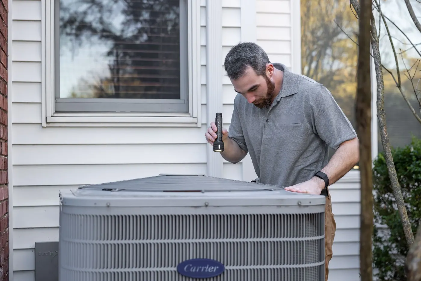 Technician checking a central AC condenser unit at a home