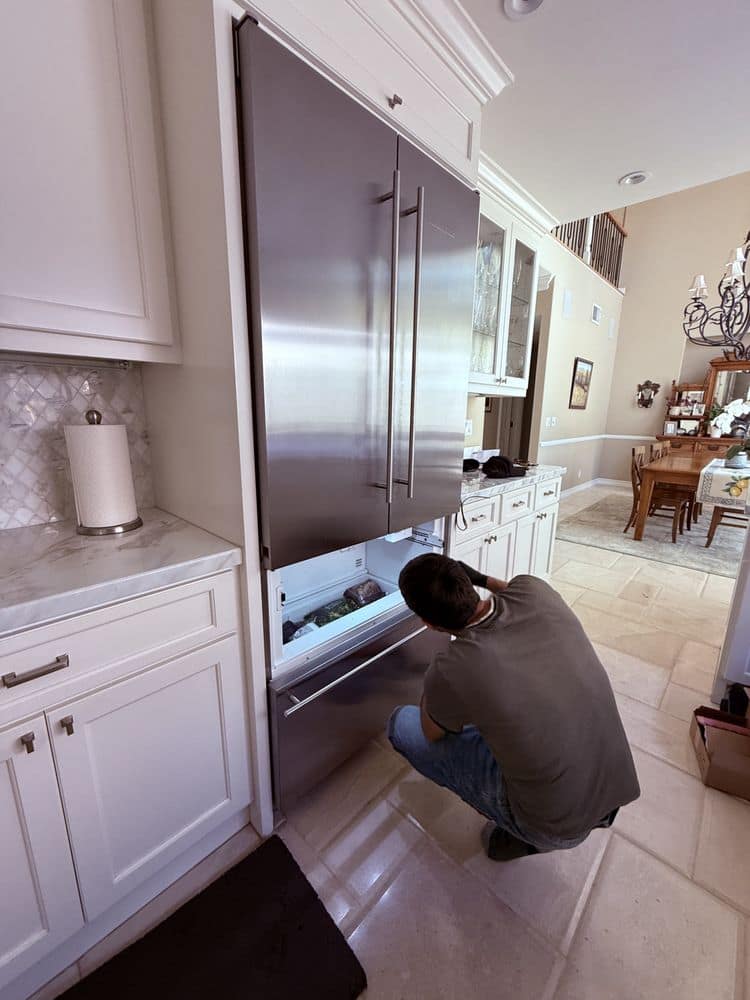 Technician servicing a built-in refrigerator panel in an Orange County kitchen